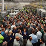 A highly detailed, high-definition photo of an unfolding dispute at an electric vehicle battery plant located in a Michigan township. The scene captures a mix of employees and management, each group with a diverse range of people. Men and women, both Caucasian and Hispanic, can be seen engaged in intense conversations amidst the high-tech battery assembly lines. Caucasian and Black employees are spotted holding banners voicing their concerns. A Middle-Eastern woman in a managerial role can be seen attempting to calm the situation.