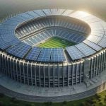 Realistic, high-definition image of a large stadium implementing green energy solutions. The stadium is creatively designed with vertical arrays of solar panels taking center stage, capturing abundant sunlight and providing sustainable power. These eco-friendly installations proudly signify the lead of the stadium in the charge towards green power.